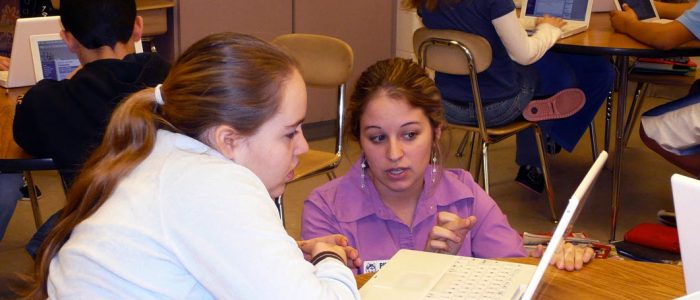 A researcher working with a young female student in a classroom.